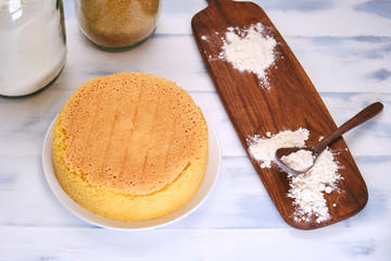 Sponge cake on a white table next to a jar of flour and sugar, preparing sweet pastries
