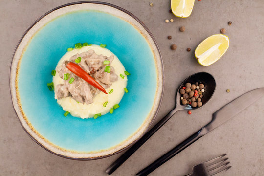 Beef Stroganoff on a blue plate, decorated with red hot pepper, is located on the table next to the Cutlery. The concept of the restaurant menu or photos for the recipes.
