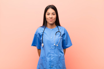young latin nurse smiling positively and confidently, looking satisfied, friendly and happy against...