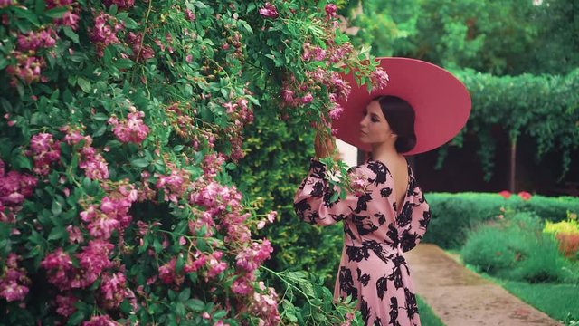 Clothes Old retro Audrey Hepburn style. Pink hat wide brimmed. Natural cosmetics concept, holiday cat eyes liner makeup, cute face sexy lips. Spring blooming garden green rose bushes. Fashion 50s 60s