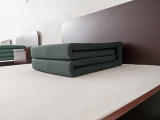perfectly folded green blanket on white sheeted bed with dark wooden headboard