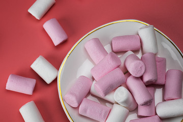 White and pink marshmallows in a saucer on a pink background.