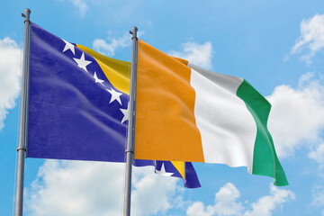 Cote D'Ivoire and Bosnia Herzegovina flags waving in the wind against white cloudy blue sky together. Diplomacy concept, international relations.