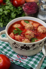 Soup with meatballs and vegetables in a bowl against a dark background