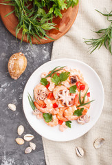 Boiled shrimps or prawns and small octopuses on white ceramic plate on a black concrete background and linen textile. Top view.