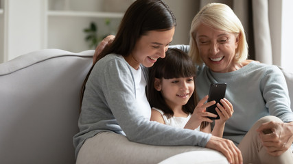 Overjoyed three generations of women laugh watching video on cell