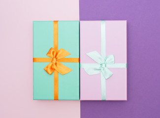 Flatlay with two colorful gift box with atlas ribbons on pink and purple background