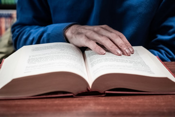 Casual man reading book on wooden table in library, vintage style