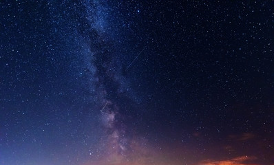 A magical starry night on the river bank with a large tree and a milky way in the sky and falling stars in the summer.	