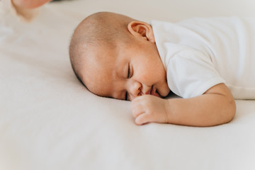 Newborn baby kid sleeping on his stomach on bed at home. Asian child bottom up sleeping position