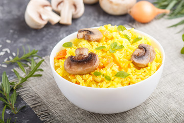 Yellow fried rice with champignons mushrooms, turmeric and oregano in white ceramic bowl on a black concrete background. side view, selective focus.
