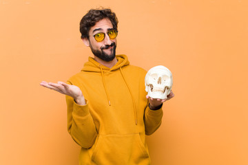 young crazy cool man holding a human skull model against orange wall