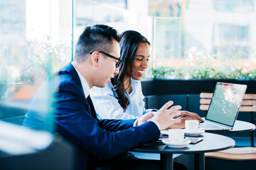 Obraz premium Cheerful adult multiracial coworkers using netbook while having hot drink in contemporary cafe