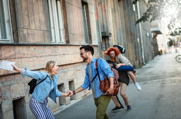 Group of smiling tourists enjoying on vacation, young friends having fun walking on city street during the day.