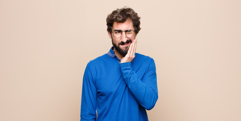 young handsome man holding cheek and suffering painful toothache, feeling ill, miserable and...
