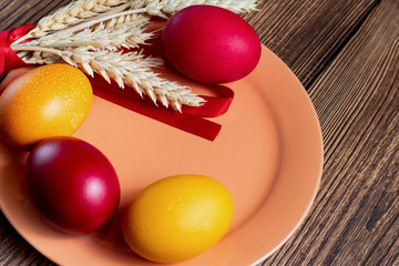 colorful eggs for Easter coral plate with ears of grain, on brown wooden background
