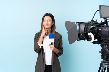 Reporter woman holding a microphone and reporting news over isolated blue background thinking an idea