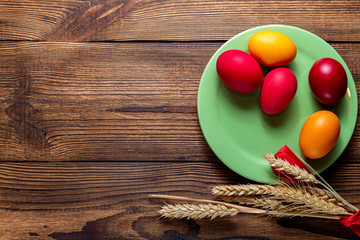 colorful eggs for Easter green plate with ears of grain, on brown wooden background
