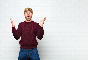 young blonde man feeling happy, excited, surprised or shocked, smiling and astonished at something...