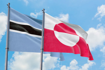 Greenland and Botswana flags waving in the wind against white cloudy blue sky together. Diplomacy concept, international relations.