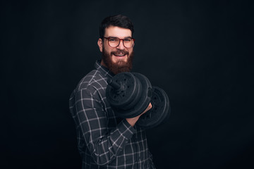 Get stronger. Yong man wearing glasses is holding a dumb-bell on dark background.