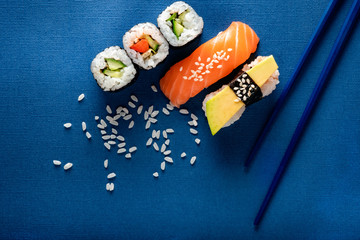 Set of sushi and rolls with salmon, avocado and cucumber on a blue background with chopsticks, top view