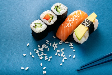 Set of sushi and rolls with salmon, avocado and cucumber on a blue background with chopsticks, top view