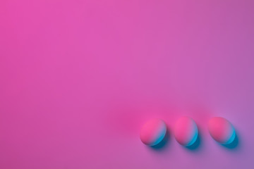 Egg hunt is coming. Easter traditions, pink-blue colored eggs on pink background, neon light, top view, copyspace for ad. Concept of holidays, spring, celebrating, food and sweets, family time.