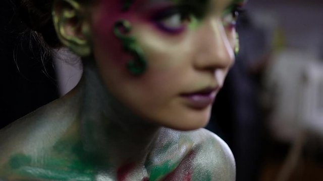 Girl in creative makeup on a black background looks into the camera and moves