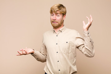 young blonde man shrugging with a dumb, crazy, confused, puzzled expression, feeling annoyed and...