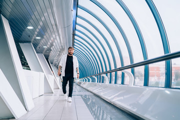 Stylish man walking with smartphone in hands along light modern tunnel