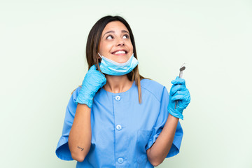 Woman dentist holding tools over isolated green background thinking an idea