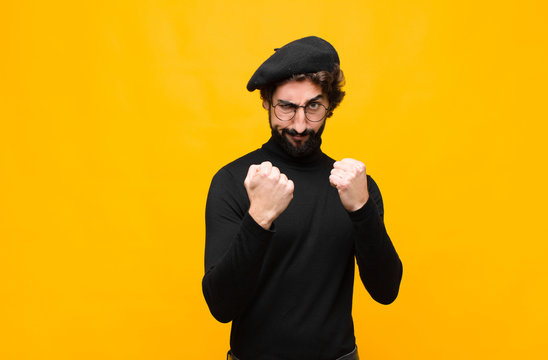 young french artist man looking confident, angry, strong and aggressive, with fists ready to fight in boxing position against orange wall