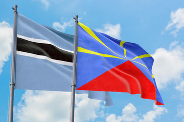 Reunion and Botswana flags waving in the wind against white cloudy blue sky together. Diplomacy concept, international relations.