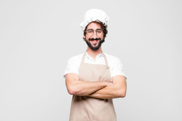 young crazy chef looking like a happy, proud and satisfied achiever smiling with arms crossed...