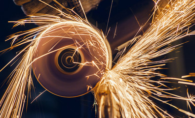 A man cuts metal using an angle grinder close-up. Many sparks