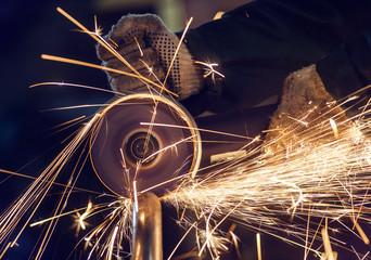 A man cuts metal using an angle grinder close-up. Many sparks