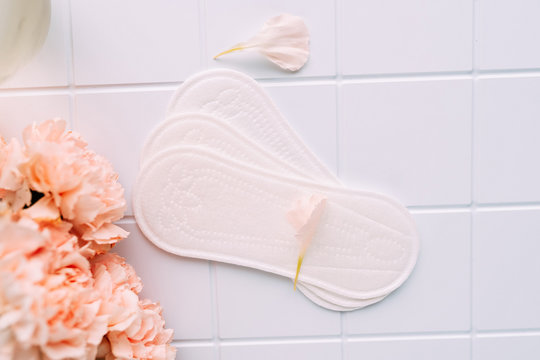 feminine hygiene products on a light background with pink flowers. flat lay of laying and flowers
