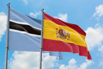 Spain and Botswana flags waving in the wind against white cloudy blue sky together. Diplomacy concept, international relations.