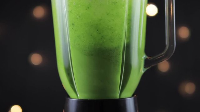 Green detox smoothie in blender on black background, super slow motion
