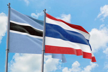 Thailand and Botswana flags waving in the wind against white cloudy blue sky together. Diplomacy concept, international relations.