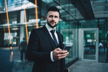 Fototapeta na wymiar Positive businessman with smartphone on street