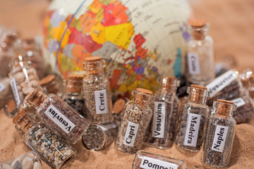 Glass test-tube with sand of different summer vacation countries. Located in sand with small globe.