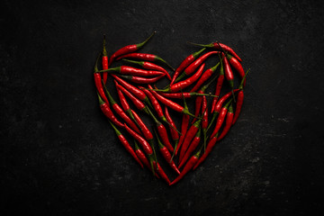 Spicy red chili pepper in the shape of a heart on a dark stone background, design concept for...