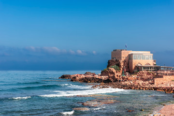 View of the blue sea in Caesarea -Israel, with part of the remains of the old biblical city, photographed in the early morning .The background is a somewhat misty bright blue sky.