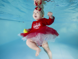 Funny little girl in red dress with toy swims underwater in a swimming pool