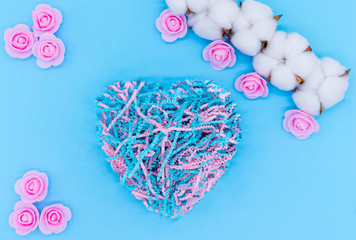 Valentine's day background. A branch of cotton and pink rose. Heart shape nest made from shredded paper on blue background.