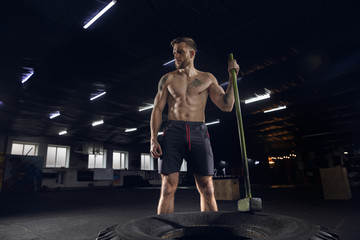 Young healthy man, athlete doing balance exercises in gym. Single model practicing hard, training hummer slam with the tire. Concept of healthy lifestyle, sport, fitness, bodybuilding, wellbeing.