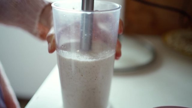 closeup female hands with hand blender making healthy dietary smoothie from raw buckwheat and apple in transparent blender cup, slow motion