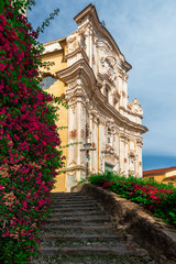 View of the streets and stairs of a small medieval village, at the top of the stairs the local church, next to the stairs a beautiful flower bush.